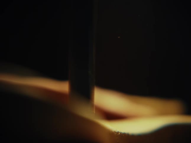 Extreme close-up in slow motion shows a drill boring a hole into wood, with sawdust erupting from the point of contact