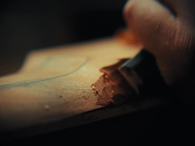 A skilled woodworker carefully carves a piece of wood with a sharp chisel in a dimly lit workshop
