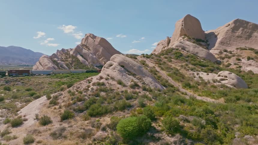 A freight train travels on tracks through a vast, arid landscape dominated by unique geological rock formations