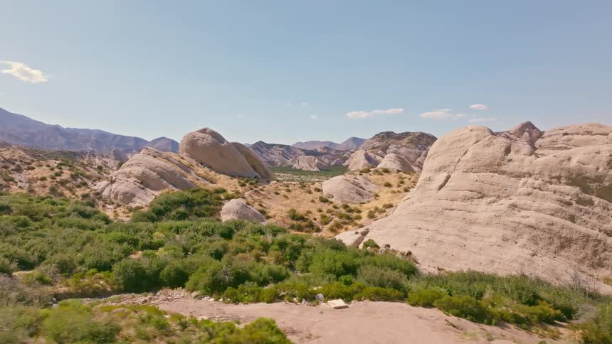 A slow aerial pull-back shot reveals the stunning and smooth rock formations in a vast, sunny desert valley