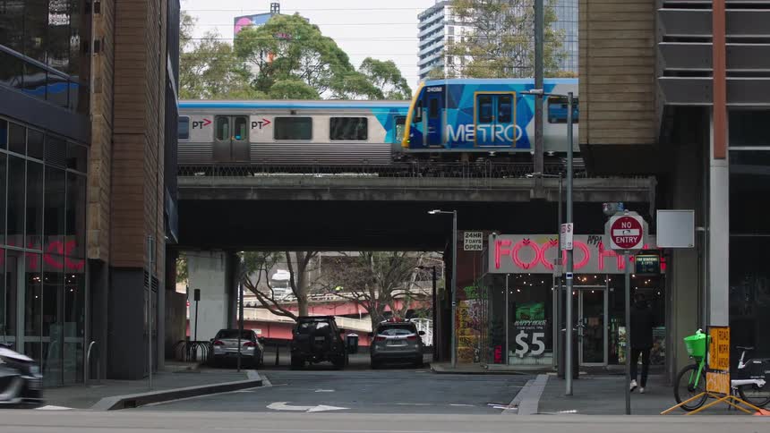 A Melbourne Metro train travels on an elevated track over a city street with traffic passing below