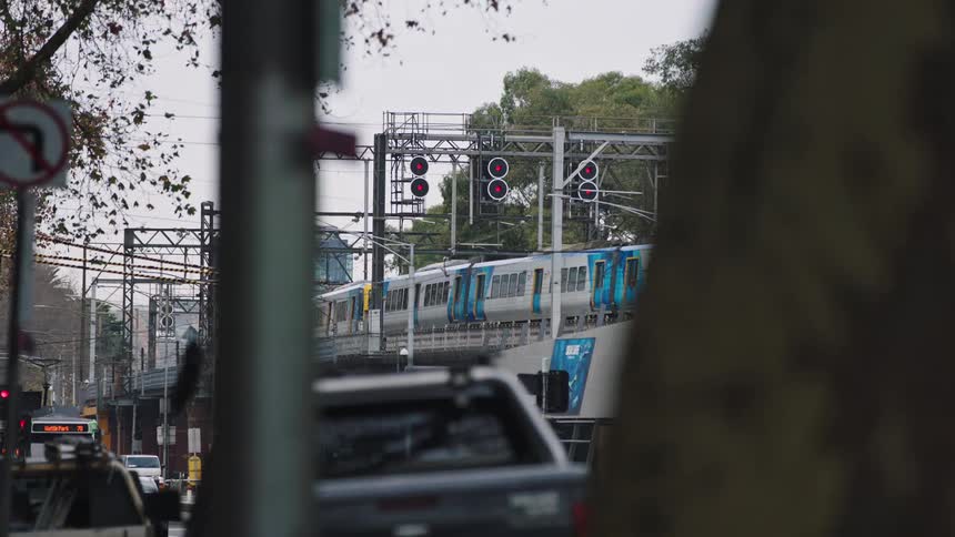 An urban commuter train on an elevated track passes red signal lights on an overcast day