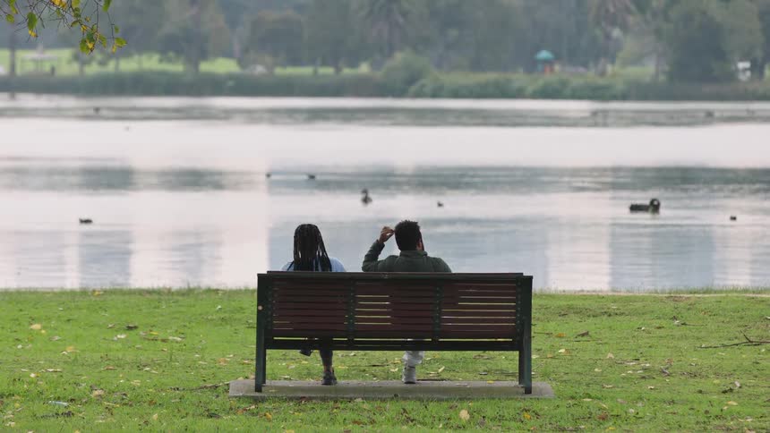 A couple sits together on a park bench enjoying the serene view of a lake with ducks swimming in the water