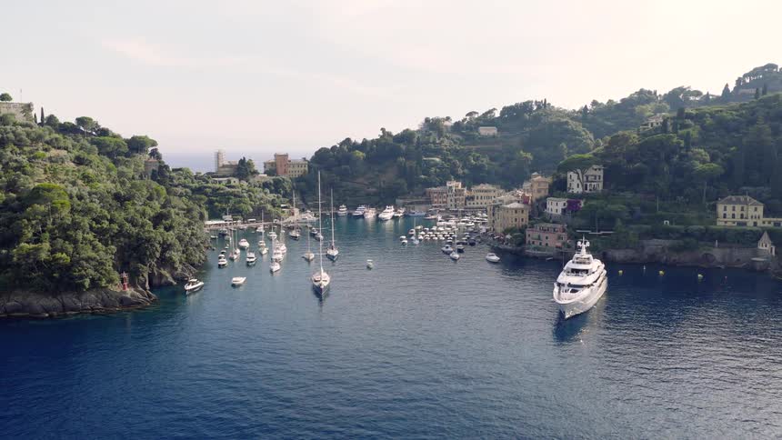 A stunning wide aerial shot of a beautiful Italian harbor filled with luxury yachts and sailboats on a sunny day