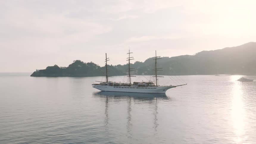An elegant white clipper ship rests peacefully on the calm ocean waters of a picturesque bay at sunrise