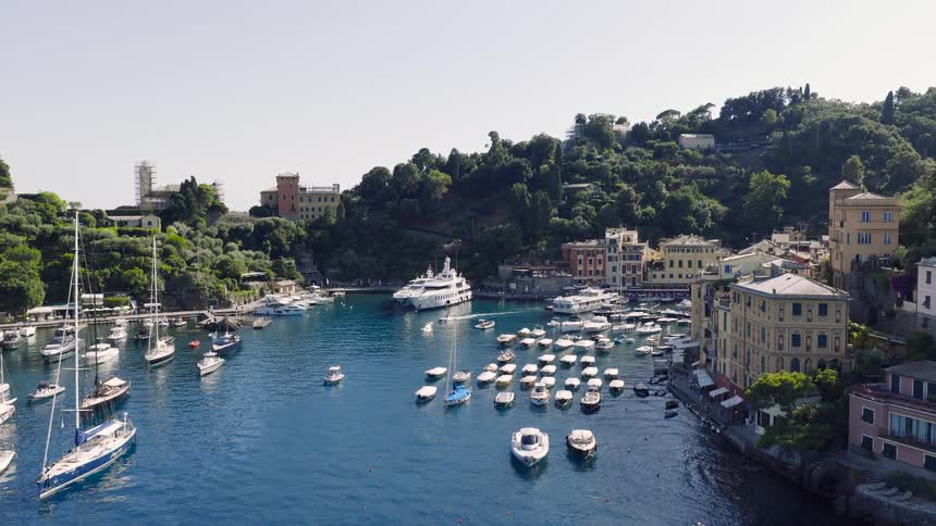 Breathtaking aerial view flying towards the famous fishing village and resort of Portofino, Italy, revealing its vibrant harbor and luxury yachts