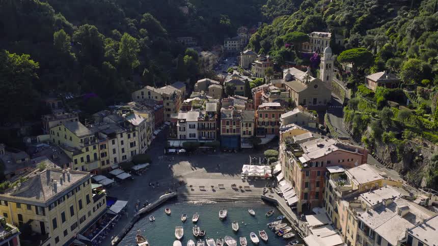 Aerial drone footage pulls back to reveal the iconic harbor and colorful village of Portofino, Italy, nestled in a lush green cove