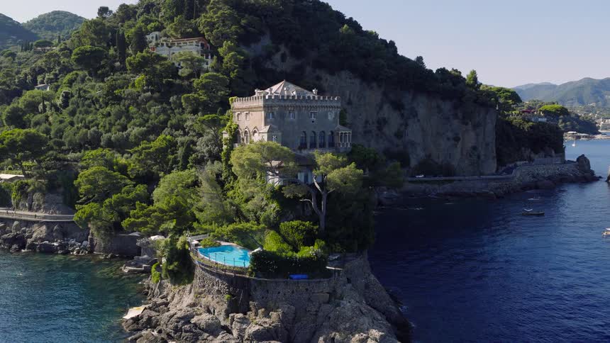 Elegant historic castle with a scenic swimming pool sits perched on a rugged cliffside above the sea along the beautiful Italian Riviera
