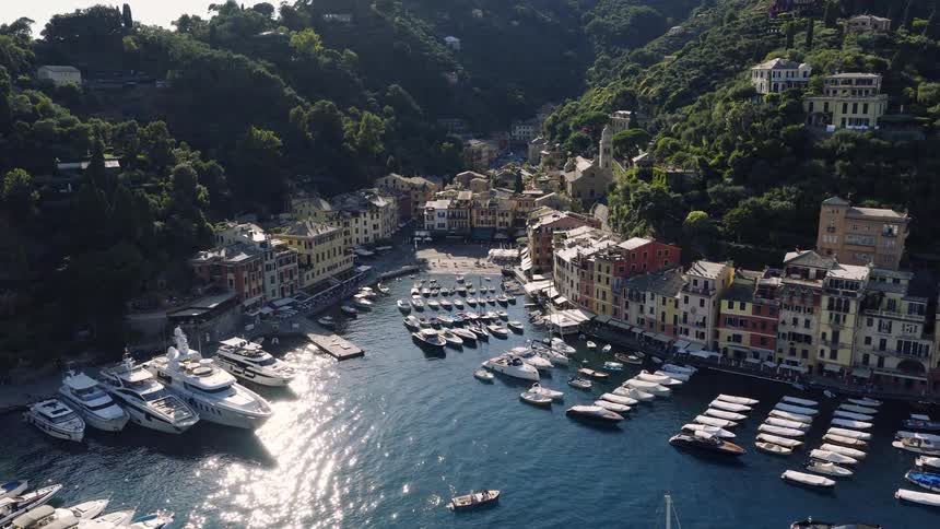 An aerial flight past Castello Brown reveals the iconic, picturesque harbor of Portofino, Italy, filled with luxury yachts and colorful buildings