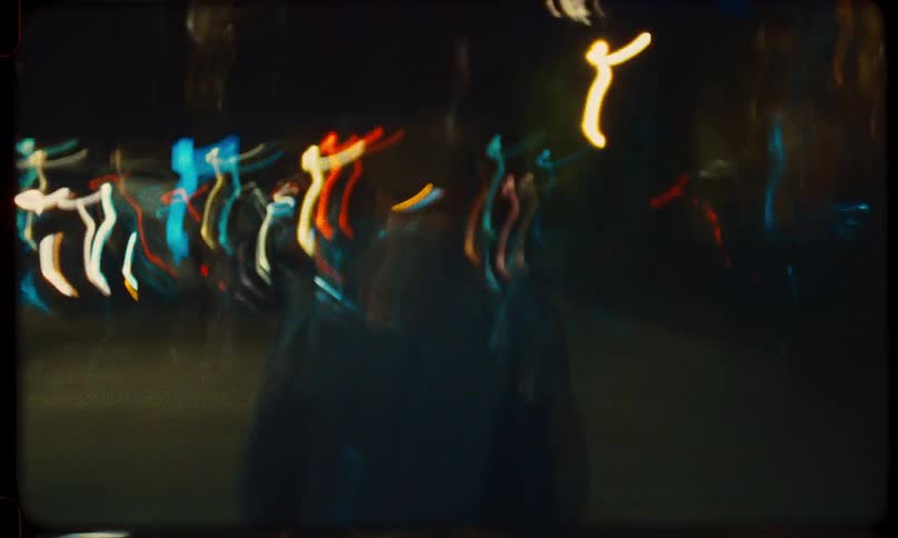 A man wearing a hat walks through a blurry, dreamlike city at night in this vintage-style experimental film