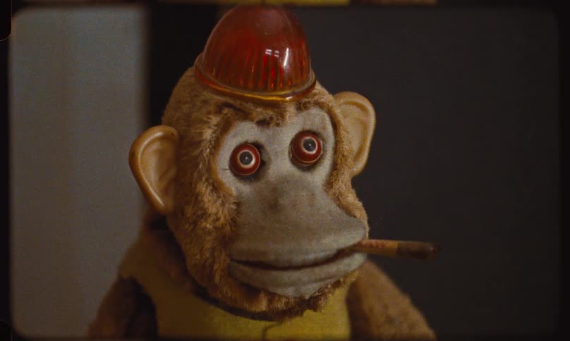 Archival Super 8 film shows a close-up of a creepy, vintage mechanical monkey toy with a cigarillo