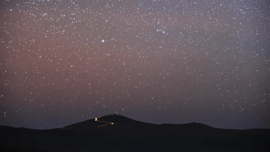 A stunning time-lapse shows the stars and Milky Way galaxy moving across the night sky above a silhouetted mountain range with an observatory on its peak