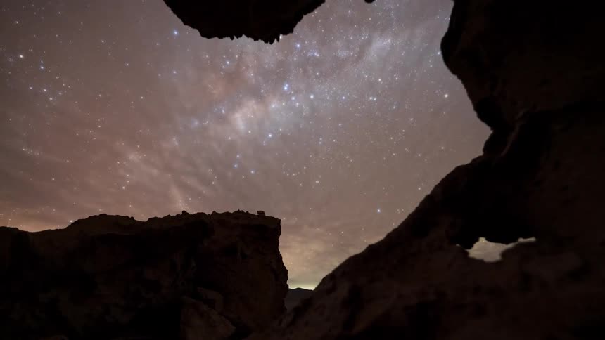 A time-lapse from a rocky cave reveals the brilliant Milky Way galaxy moving across the night sky until clouds roll in to cover the stars
