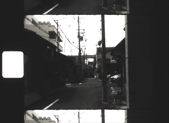 Gritty black and white 8mm film of a quiet, empty residential alleyway in Japan with telephone poles and power lines