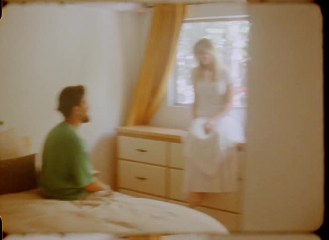 Retro-style footage captures a tender moment between a young couple talking in their sunlit bedroom