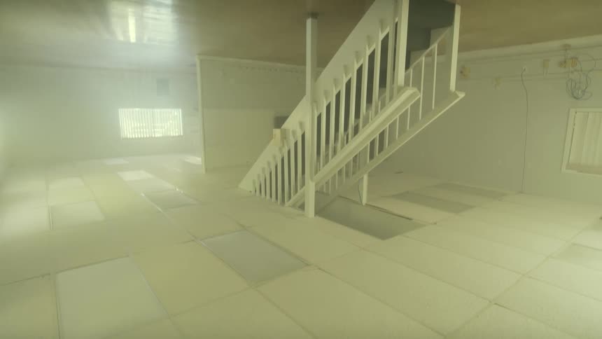 Disorienting upside-down shot slowly reveals a vacant, sterile room with a staircase and tiled ceiling