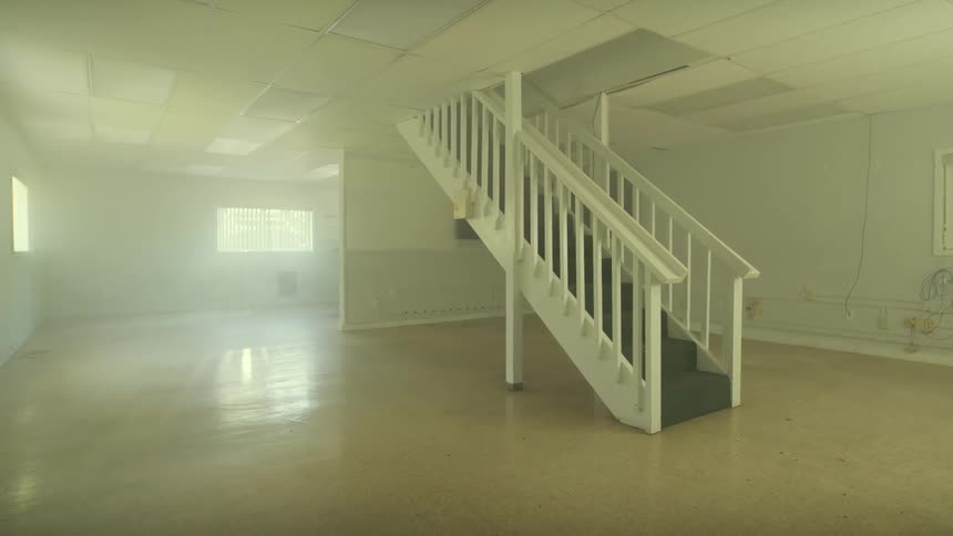 A slow pan reveals a hazy, empty, and abandoned commercial office space with a staircase in the middle of the room