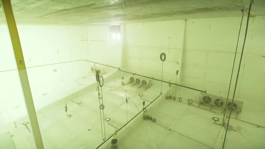 High-angle view of a large, empty, and eerie industrial room with flickering lights as the camera slowly pans up to the ceiling