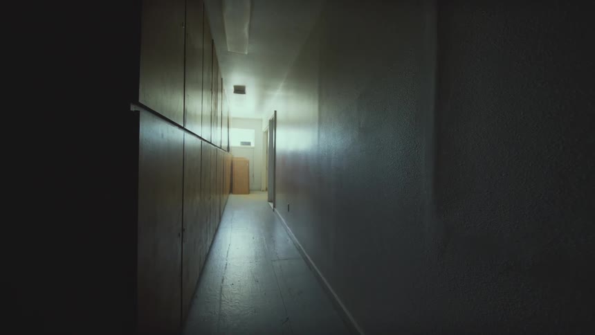 A slow pan across a long, dark, and empty hallway lined with wooden cabinets creates a creepy and suspenseful atmosphere