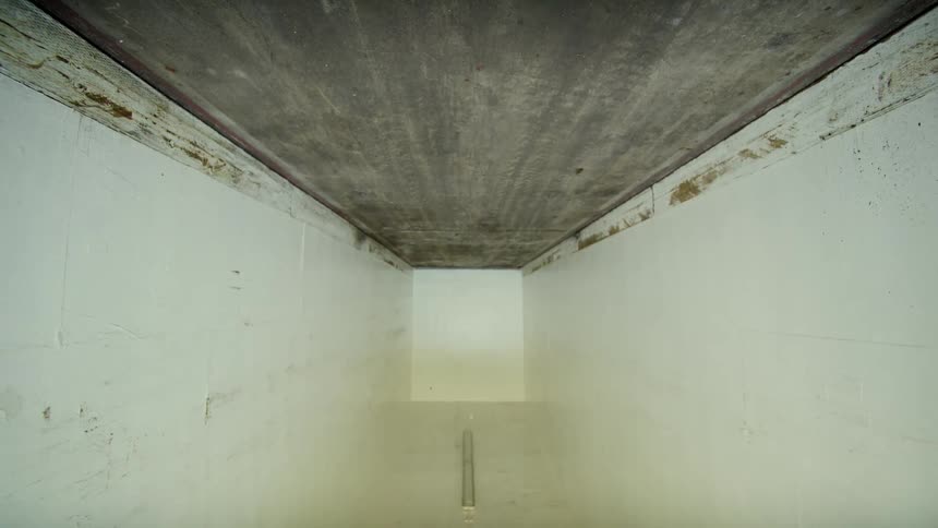 A slow camera zoom out from a dirty concrete ceiling reveals a stark, empty white room