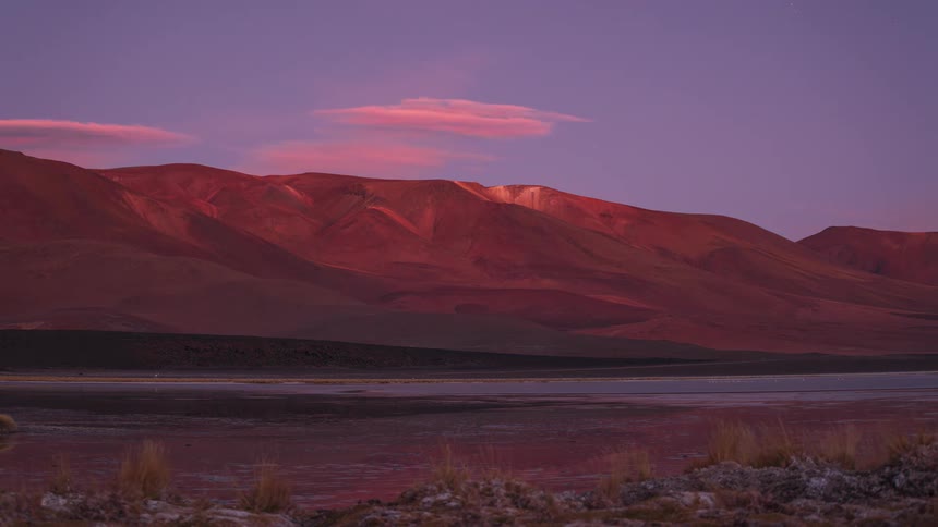 Vibrant sunset and alpenglow give way to a starry night sky in a breathtaking timelapse over a tranquil lake and red mountains