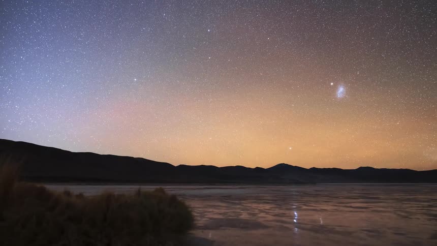 A stunning timelapse captures the transition from a starry night sky with the Milky Way to a vibrant sunrise over a vast desert salt flat and mountains