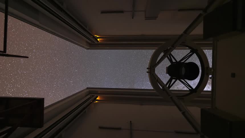 Time-lapse looking up from inside an observatory as the roof opens at dusk, revealing the Milky Way and stars traversing the night sky as a telescope observes