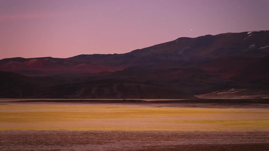 A stunning day-to-night timelapse captures the sunset and moonrise over a colorful arid landscape with dramatic mountains and a starry night sky
