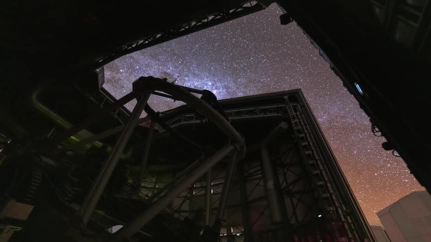 A low-angle timelapse of a large telescope in an observatory opening up to reveal the Milky Way and stars moving across the night sky