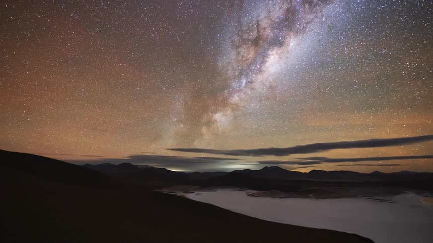 A stunning day-to-night-to-day time-lapse shows the Milky Way rising over a vast mountain landscape and salt flat, eventually transitioning back to sunrise
