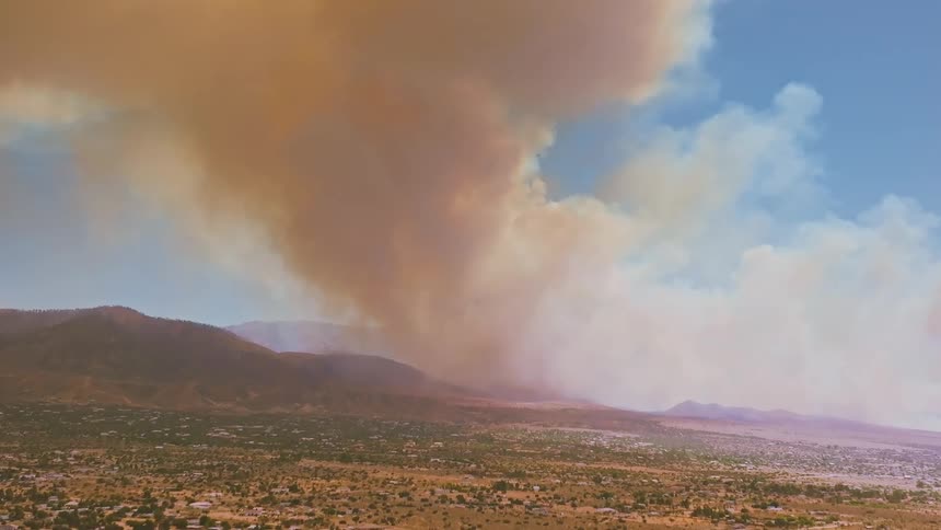 An ominous fire tornado swirls above a vast desert landscape as a wildfire rages in the mountains