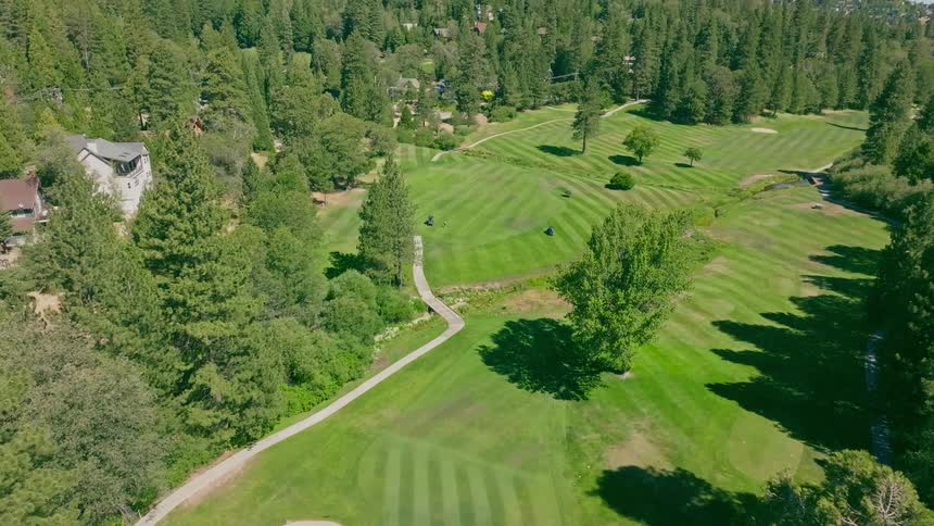 An aerial view starts above a perfectly manicured golf green and slowly rises to reveal a stunning golf course nestled in a lush, green mountain valley