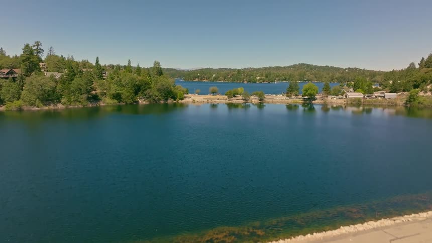 Aerial view flying up a rock-faced dam to reveal the beautiful blue waters of Lake Arrowhead on a sunny day