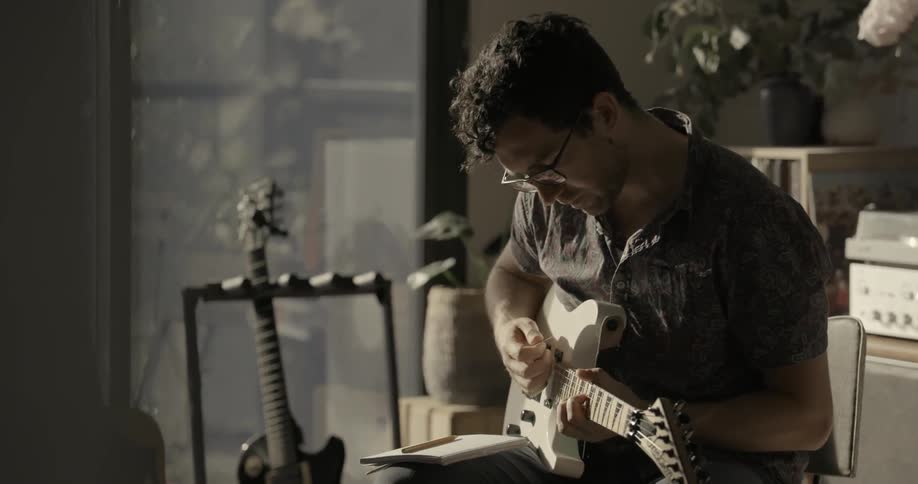 A man sits writing then plays the guitar