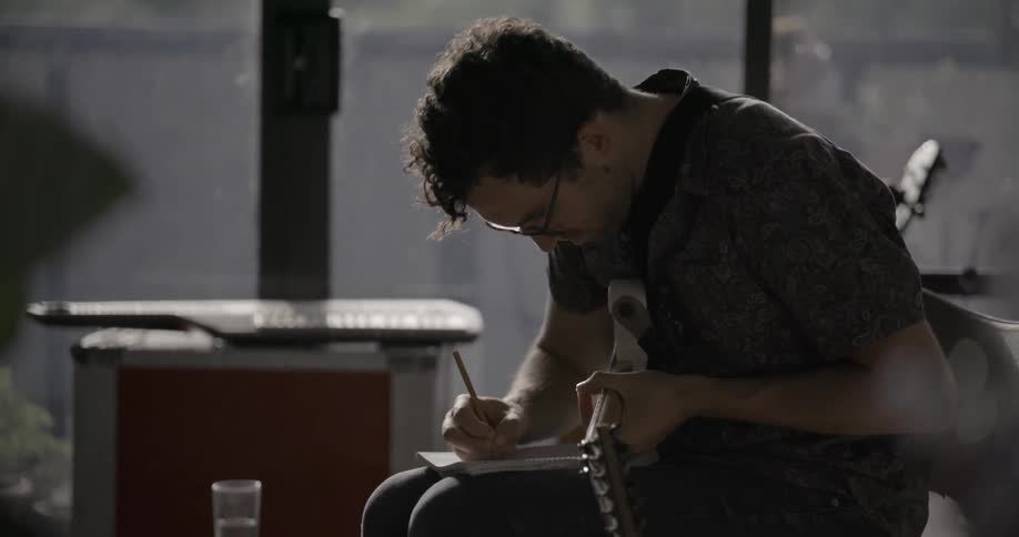 A man is playing a guitar and taking composition notes