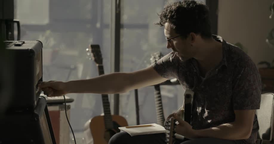 A man plays guitar and adjusts his amplifier