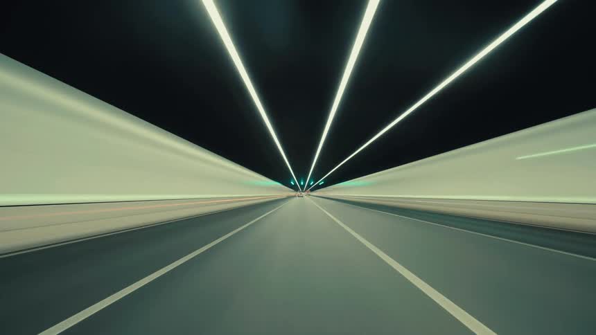 A dynamic first-person perspective time-lapse captures the exhilarating rush of driving through a brightly lit, modern highway tunnel at night