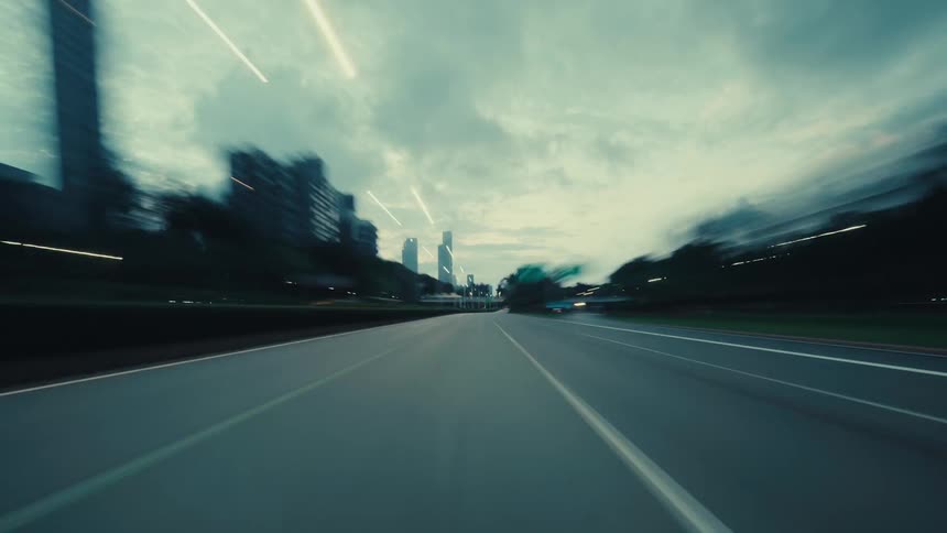 A futuristic point-of-view hyperlapse captures the experience of driving down a city highway at dusk as lights streak past in a blur