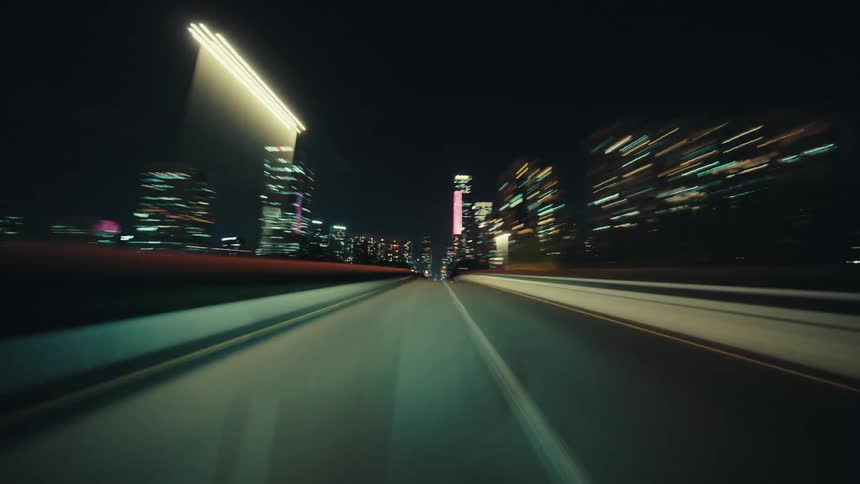 A dizzying hyperlapse from a car driving down an empty highway at night through a modern city with glowing skyscrapers