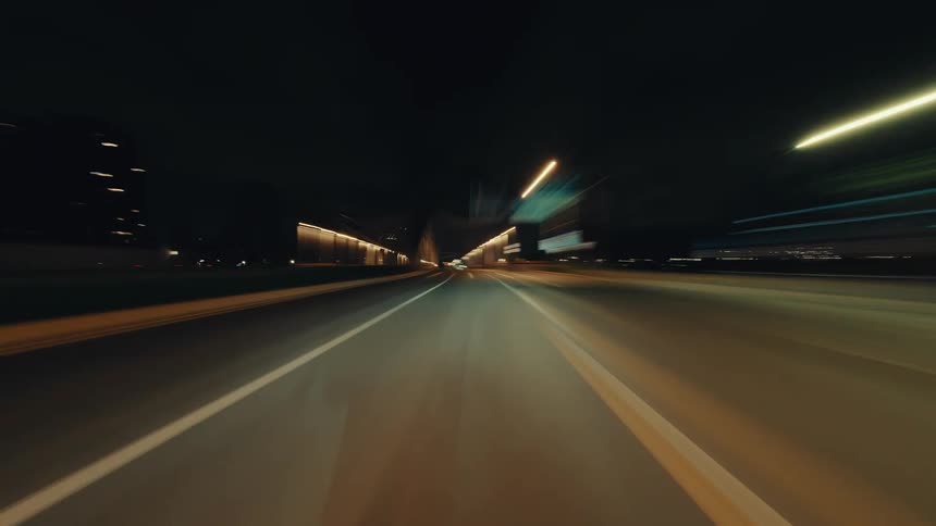 A thrilling first-person-view hyper-lapse captures a high-speed drive through a city at night, creating mesmerizing light trails