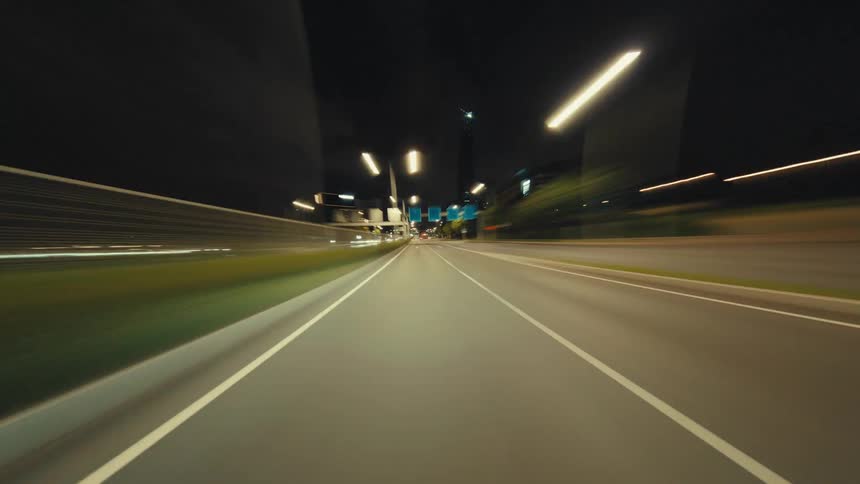 A dynamic first-person point-of-view time-lapse driving at high speed through an illuminated tunnel and onto a city highway at night