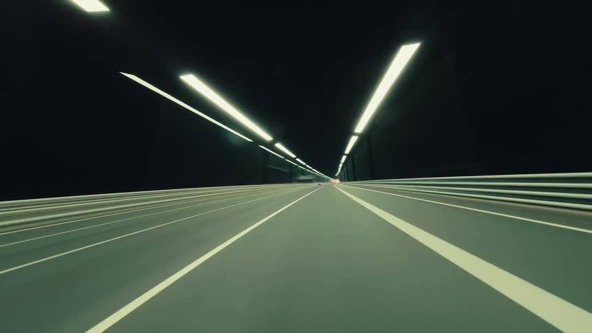A first-person perspective time-lapse captures streaks of light while driving through a dark city tunnel at night