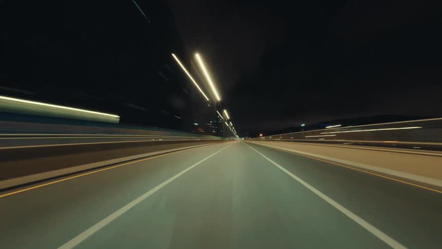 A surreal point-of-view hyper-lapse of driving at high speed on a city highway at night, with lights streaking past