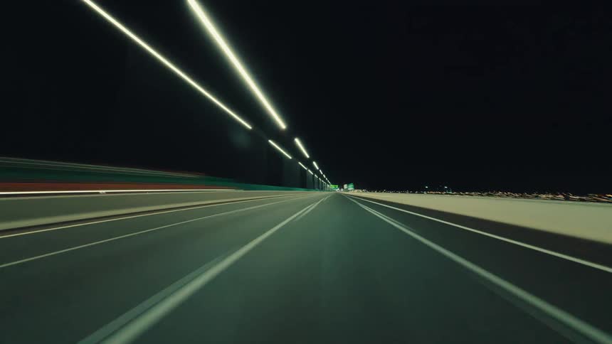 A futuristic first-person point-of-view timelapse of driving down an illuminated highway at night, creating mesmerizing light trails