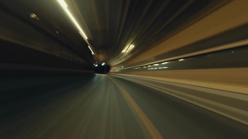 A high-speed time-lapse journey through a brightly lit highway tunnel at night, creating mesmerizing light trails