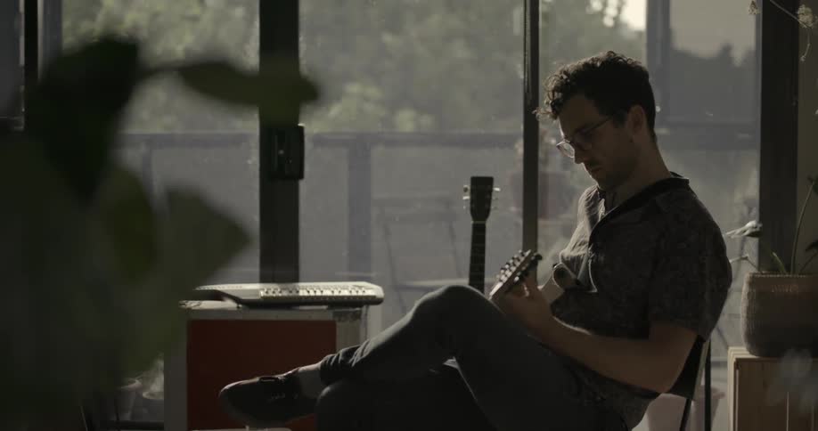 A man is playing a song on the guitar while seated in a chair