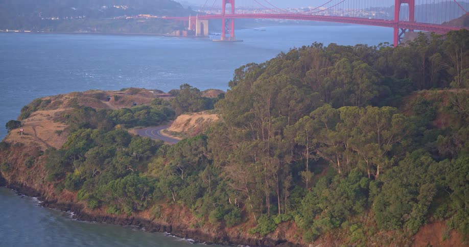 A scenic reveal of the iconic Golden Gate Bridge from behind the tree-covered Marin Headlands coastline