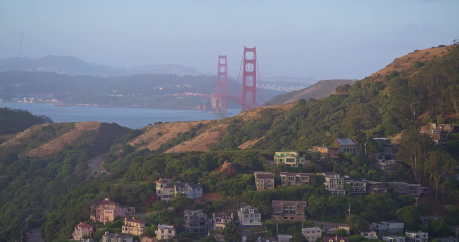 A scenic view of the iconic Golden Gate Bridge from the lush, residential hills of Sausalito during a hazy morning