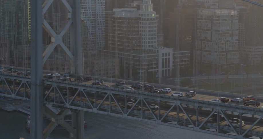 Commuters drive across the iconic San Francisco Bay Bridge with the hazy city skyline in the background during golden hour