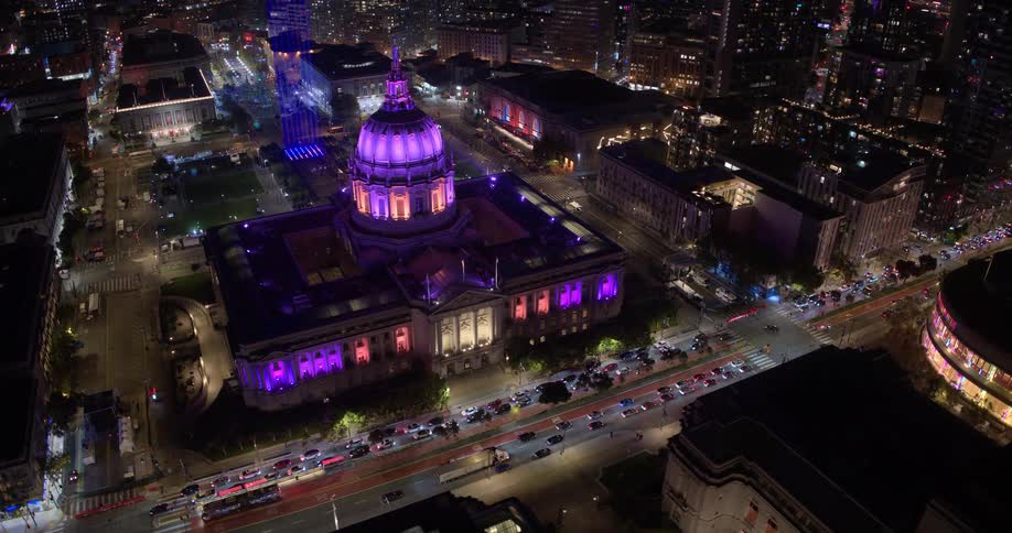 Stunning night aerial view of San Francisco City Hall, illuminated in brilliant purple lights, as traffic streams by in the bustling city